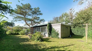 A small wooden cabin with a glass enclosure, surrounded by a well-maintained garden and trees. - Child-friendly Garnekuul 81 Bungalow (Callantsoog)