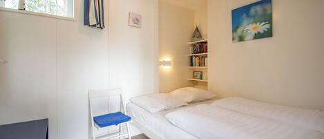 A bedroom with a bed, a chair, a bookshelf, and a window with curtains.