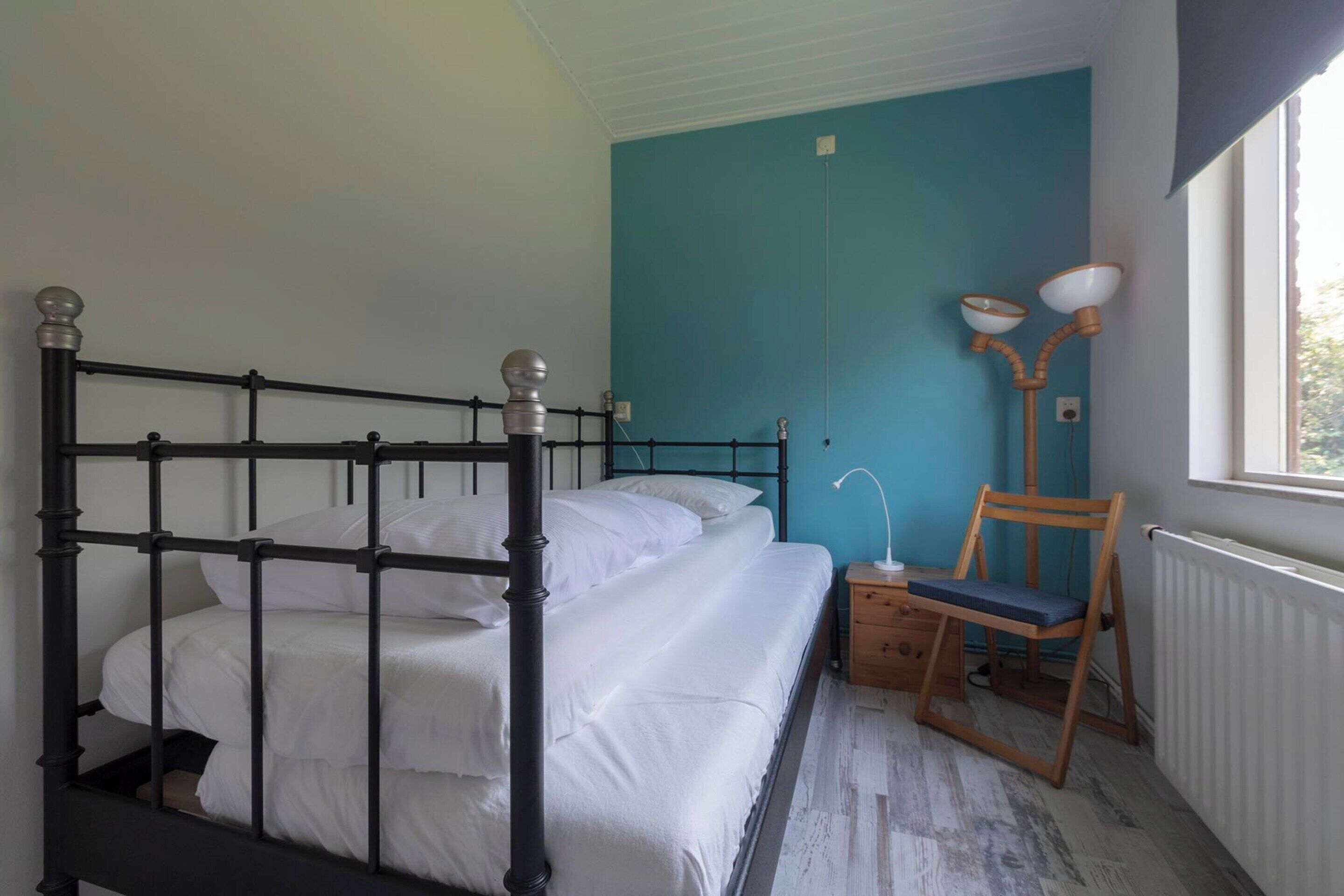 A bedroom with a bed, a chair, a nightstand, and a window.