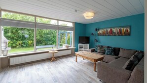 Un salon avec une grande fenêtre, une table en bois, un canapé et un tableau accroché au mur.