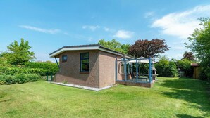 Une petite maison en briques dotée d’une véranda en verre, entourée d’une pelouse bien entretenue et d’arbres.