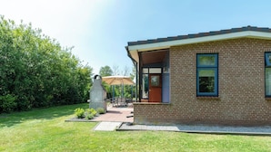 Une maison moderne en briques, dotée d’un patio couvert, d’une sculpture en pierre et d’un jardin.