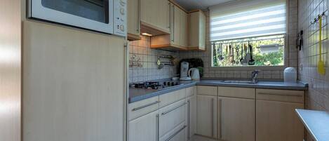 Una cocina compacta con horno empotrado, cocina a gas y ventana con persianas.