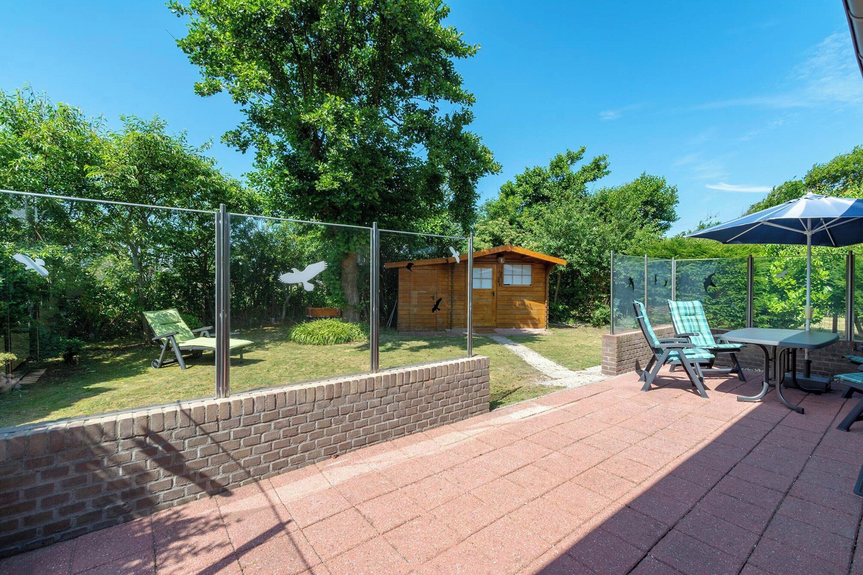 A patio area with a table and chairs, a small wooden structure, and a glass fence.