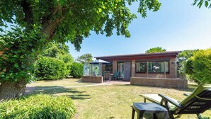 A modern house with a patio, a table, and a chair. - Bungalow at Garnekuul Park With Garden (Callantsoog)
