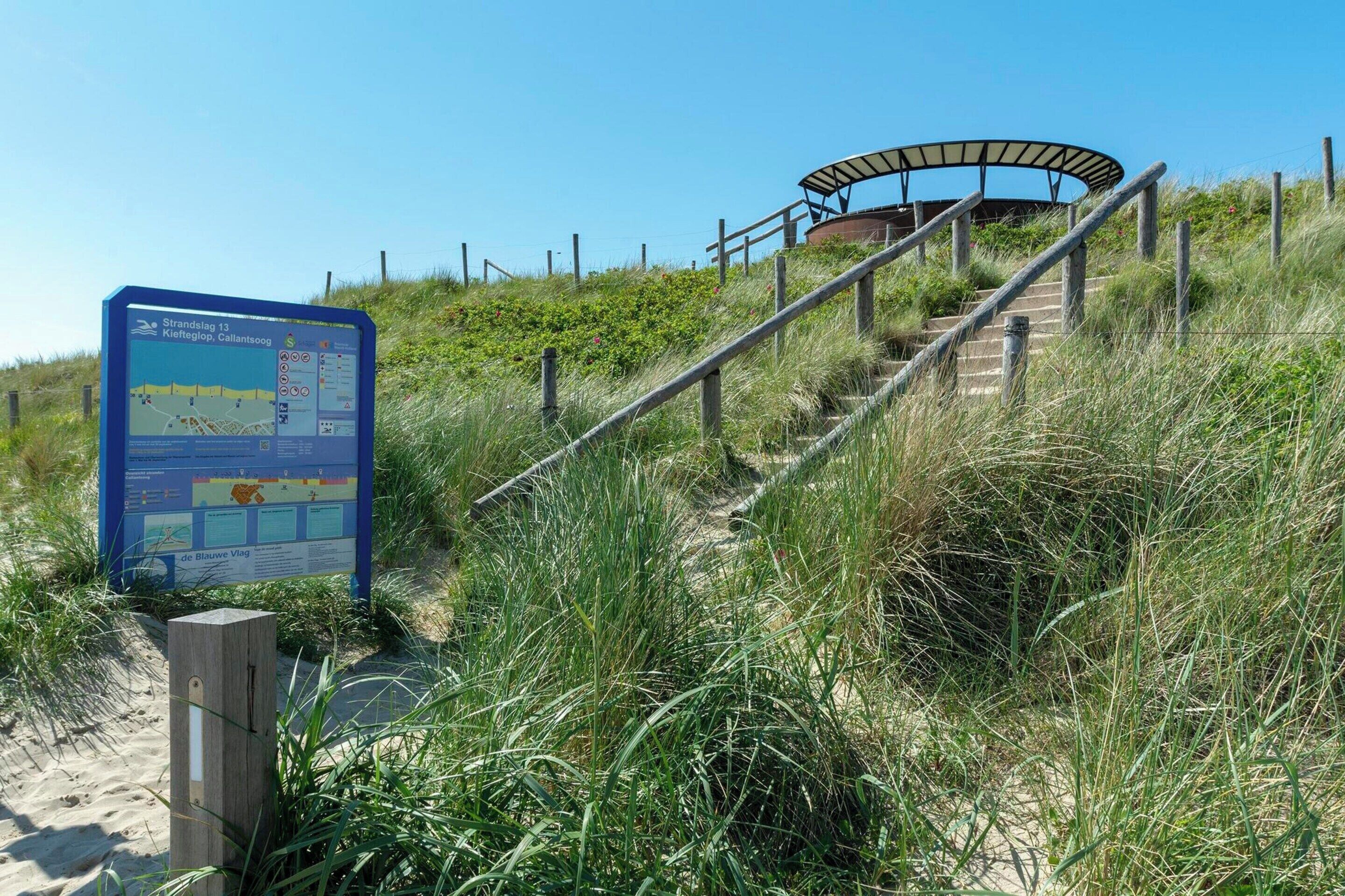 Ein Strandweg mit einem Schild, Holzstufen und einer Schutzhütte.