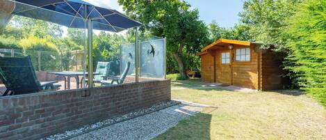 A patio area with a glass enclosure, outdoor furniture, and a wooden cabin.