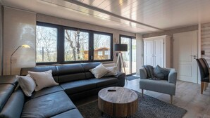 A modern living room with a sectional sofa, a round coffee table, and a grey armchair. - Bungalow at Garnekuul Park With Garden (Callantsoog)