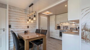 A modern kitchen with white cabinets, a wooden dining table, and pendant lights. - Bungalow at Garnekuul Park With Garden (Callantsoog)