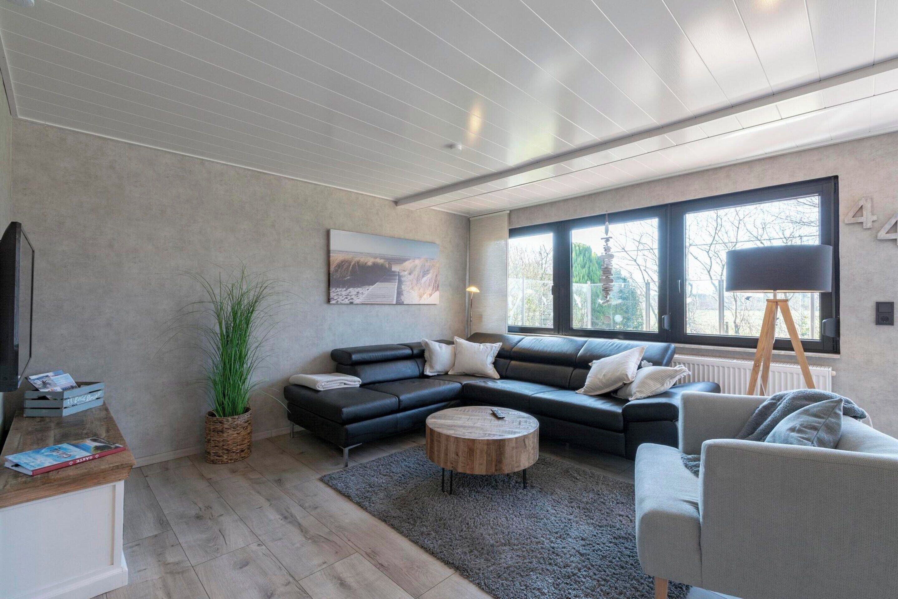 Un salon moderne avec un canapé d’angle, une table basse ronde et une grande fenêtre qui laisse entrer la lumière naturelle.
