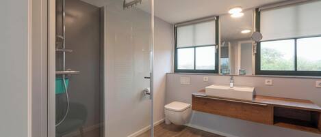 A modern bathroom with a glass-enclosed shower, a toilet, a sink with a wooden vanity, and a large window providing natural light.