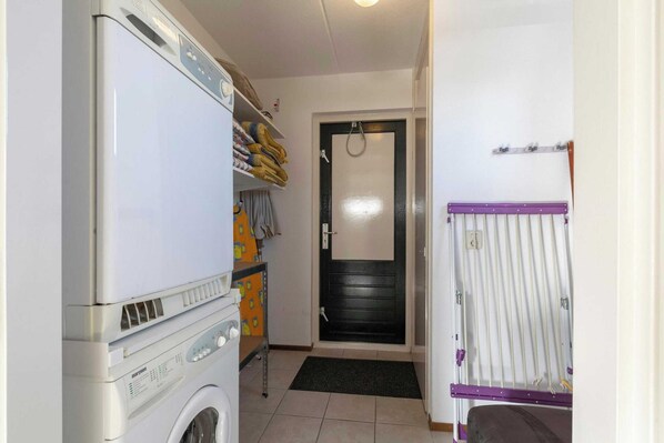 Une buanderie équipée d’un lave-linge, d’un étendoir et d’étagères où sont pliées les serviettes.
