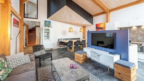 A modern living room with a sofa, coffee table, and TV. There is a dining area with a table and chairs. The room has wooden beams and a large window. - Villa Near Sint Maartenszee Beach With Jacuzzi (Sint Maartensvlotbrug)