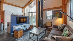 A spacious living room with a large TV, wooden beams, a fireplace, and a sofa with cushions. - Villa Near Sint Maartenszee Beach With Jacuzzi (Sint Maartensvlotbrug)
