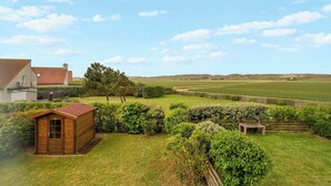 A wooden shed, a wooden bench, and a fenced area in a well-maintained grassy field with a house in the background. - Villa in Julianadorp Near Sandy Beach (Julianadorp)