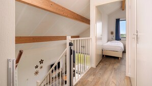 A bedroom with a bed, a wooden staircase, and a view of the outdoors. - Villa in Julianadorp Near Sandy Beach (Julianadorp)