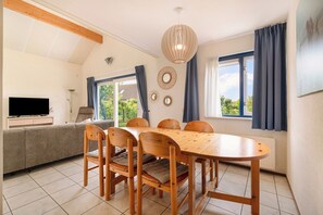 A dining area with a wooden table and chairs, a sofa, and a television. - Villa in Julianadorp Near Sandy Beach (Julianadorp)
