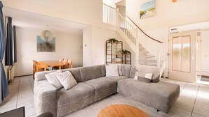 A living room with a sectional sofa, a dining table, and a staircase. - Villa in Julianadorp Near Sandy Beach (Julianadorp)