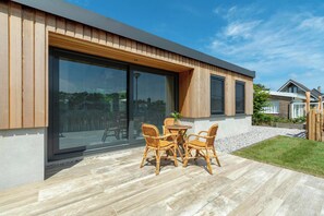 A modern house with large sliding glass doors, a patio with a table and chairs, and a well-maintained lawn. - Attractive Home With Terrace (Callantsoog)