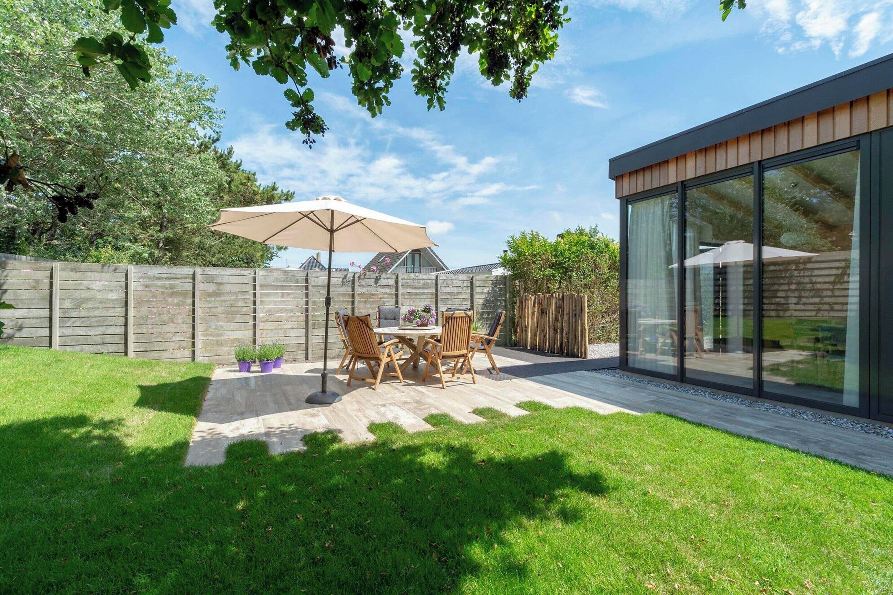 Eine moderne Terrassengrundstück mit Tisch und Stühlen, einem großen Sonnenschirm und einem Holzzaun.