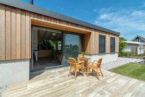 A modern house with a wooden exterior, a glass door leading to an interior space, and a patio with wicker furniture. - Attractive Home With Terrace (Callantsoog)
