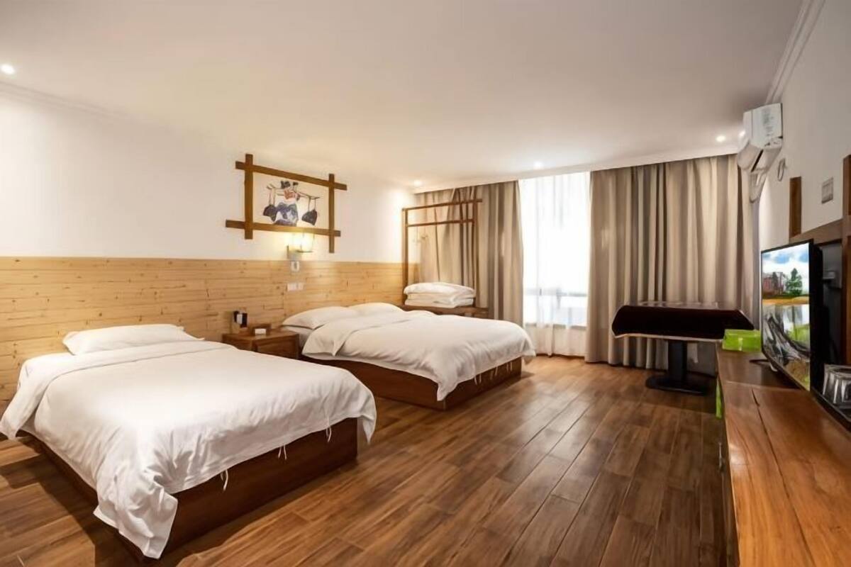 Ein Hotelzimmer mit zwei Betten, einem Holzkopfteil, einem Flachbildfernseher und einem großen Fenster mit Vorhängen.