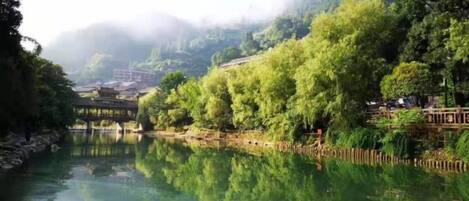 A river with a bridge, surrounded by lush greenery and a misty mountain backdrop.
