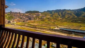 Une vue depuis un balcon donnant sur des rizières en terrasses et un village aux bâtiments traditionnels.