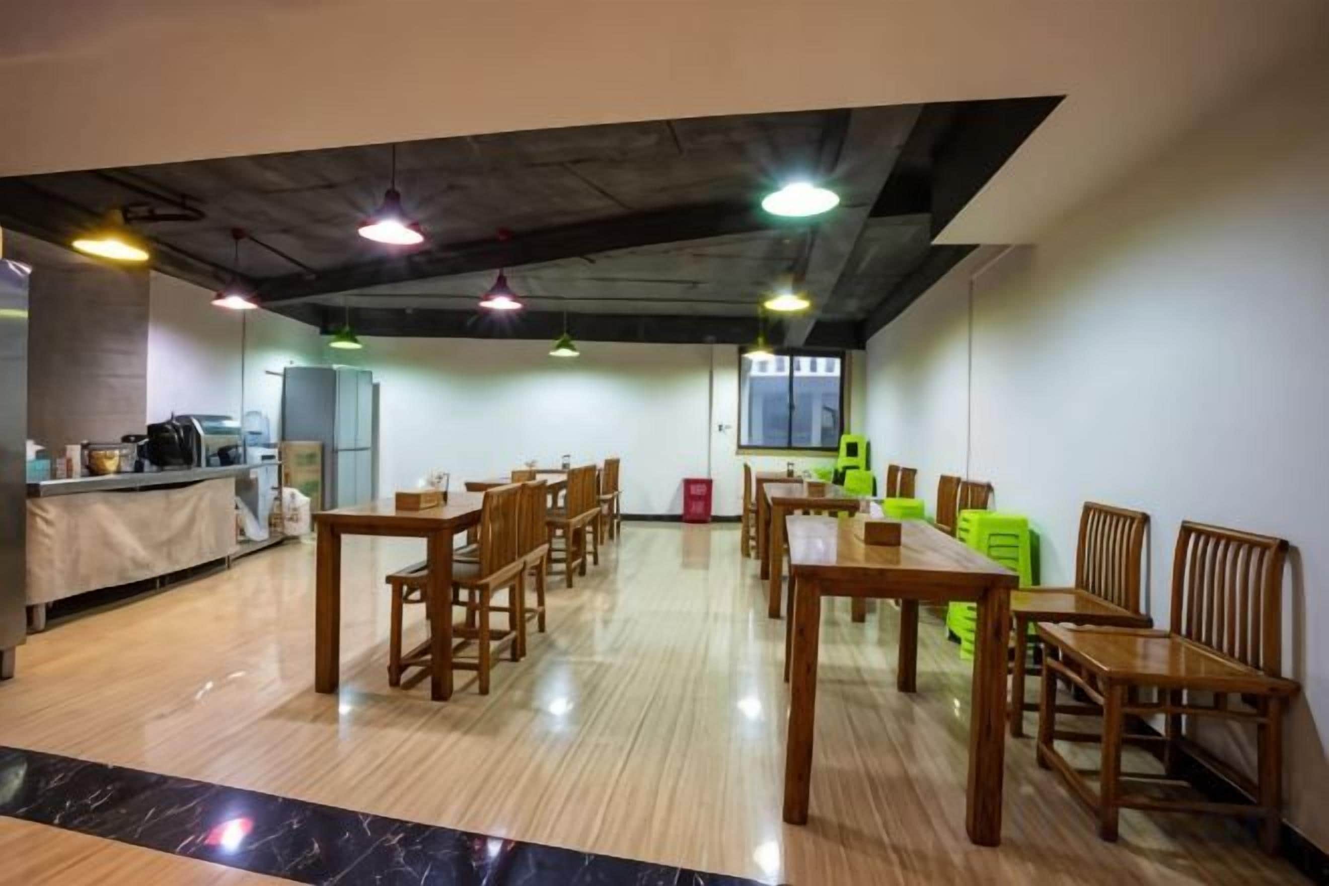 A dining area with wooden tables and chairs, a kitchen in the background, and a view of the outside.