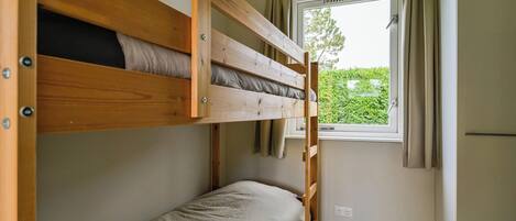 A bunk bed room with a window and curtains, a small kitchenette, and a view of greenery outside.