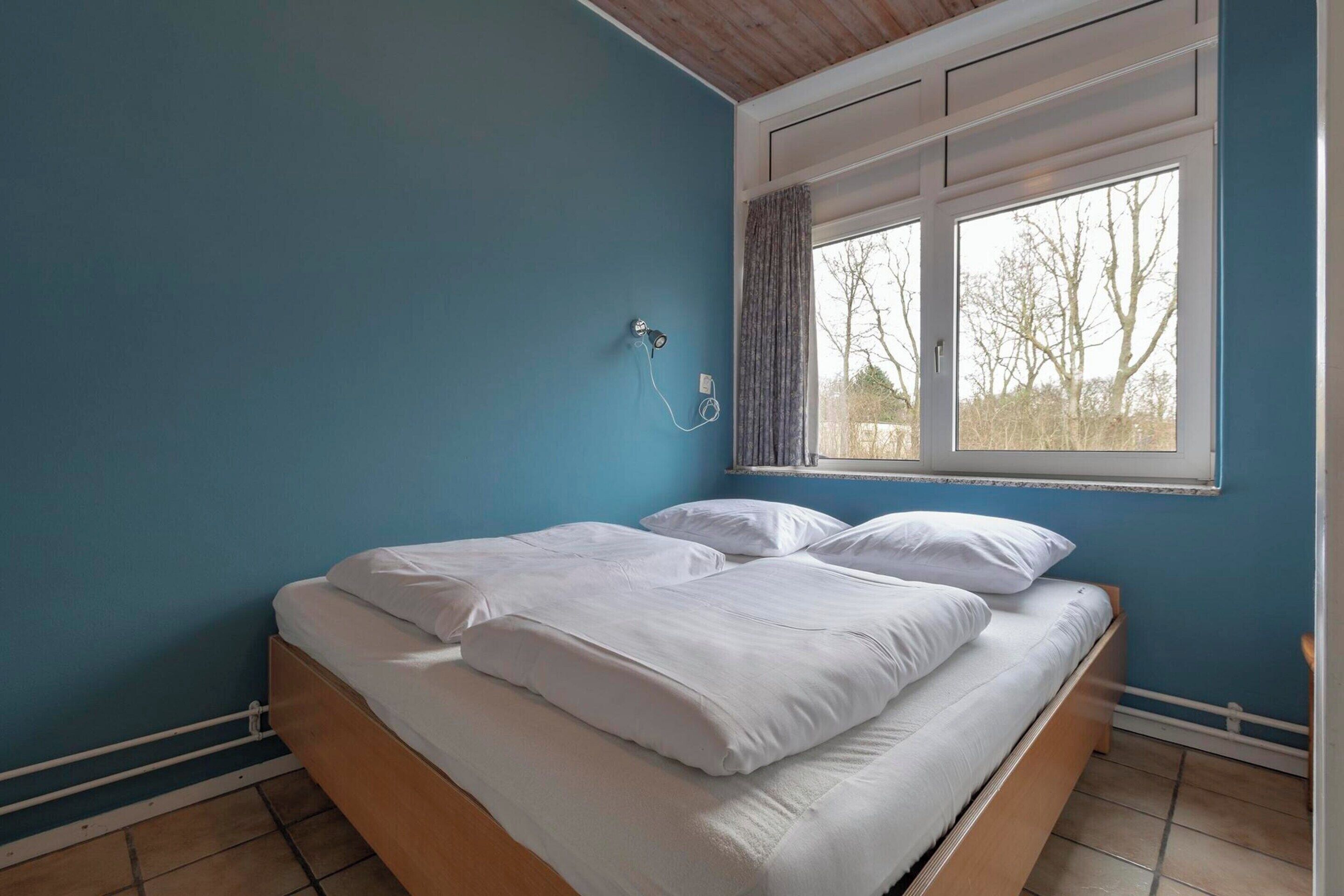 A bedroom with a single bed, a window with curtains, and a wall-mounted heater.