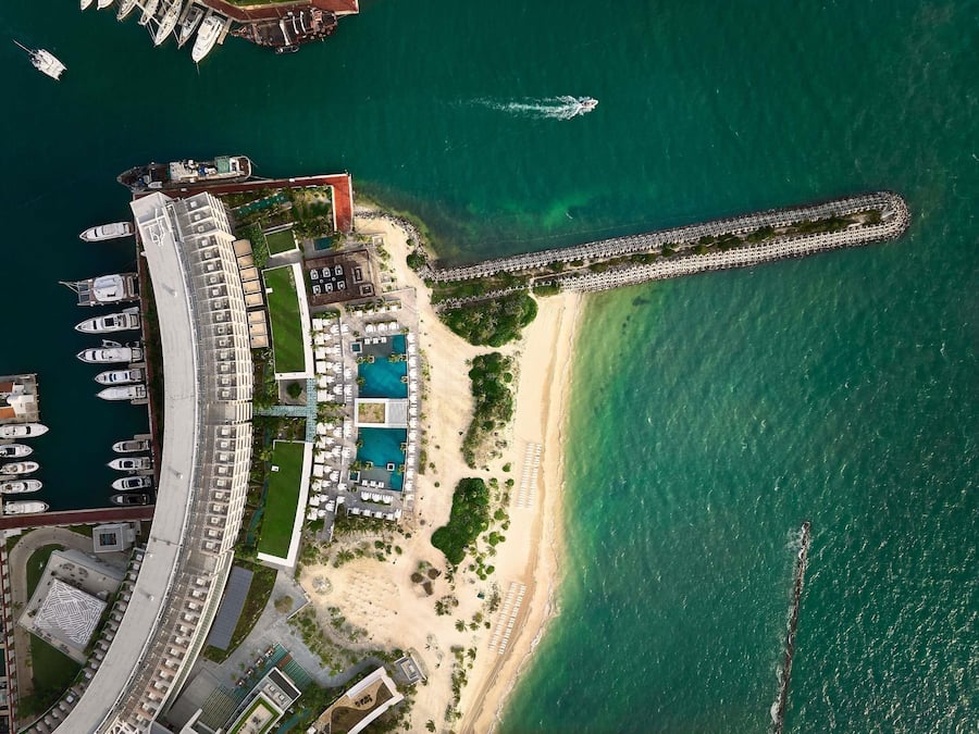 An aerial view of a coastal resort with a marina, swimming pools, and a long pier.