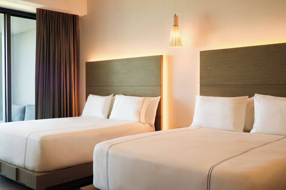 Habitación de hotel con dos camas, un ventanal con cortinas y una lámpara colgante.
