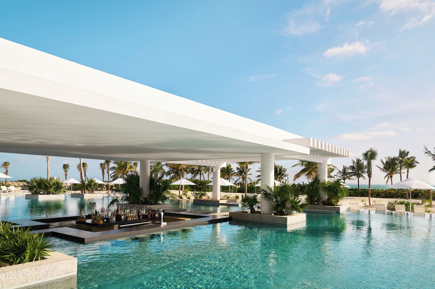 A modern pool area with clear water, palm trees, and a covered walkway.