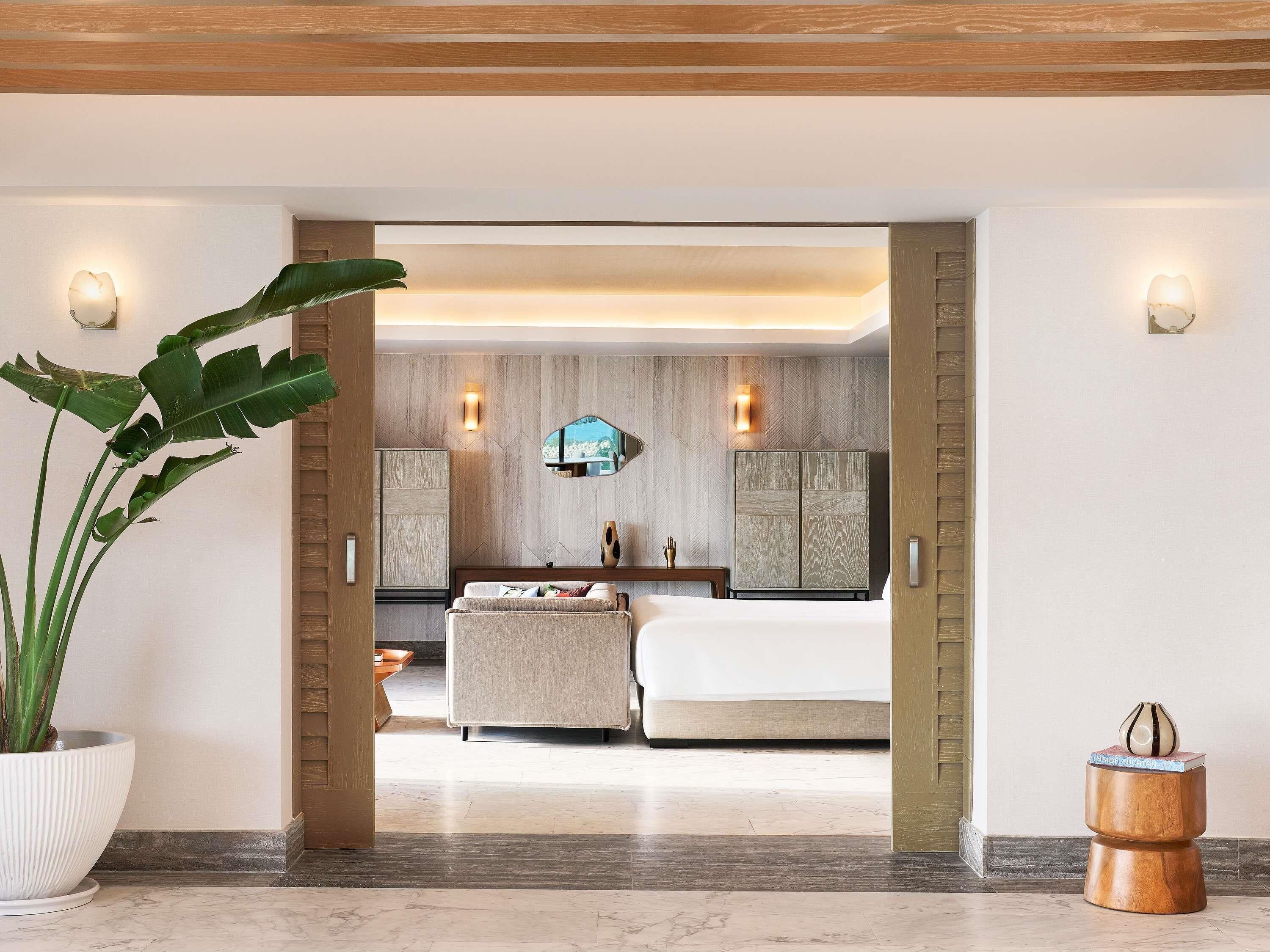 A modern hotel room with a large bed, a seating area, and a view of the city.