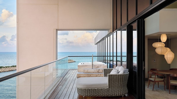 Un balcón con vistas al mar, una zona de estar con cojines y una mesa de comedor con sillas.
