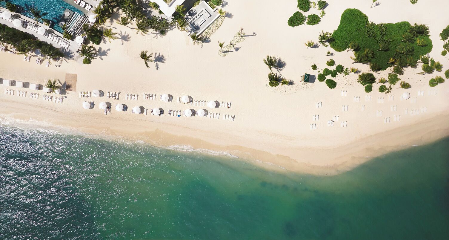 Vista aérea de una playa con filas de tumbonas, un área de piscina y una pequeña zona verde con plantas.