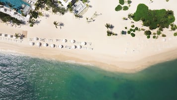 Vista aérea de una playa con filas de tumbonas, un área de piscina y una pequeña zona verde con plantas.
