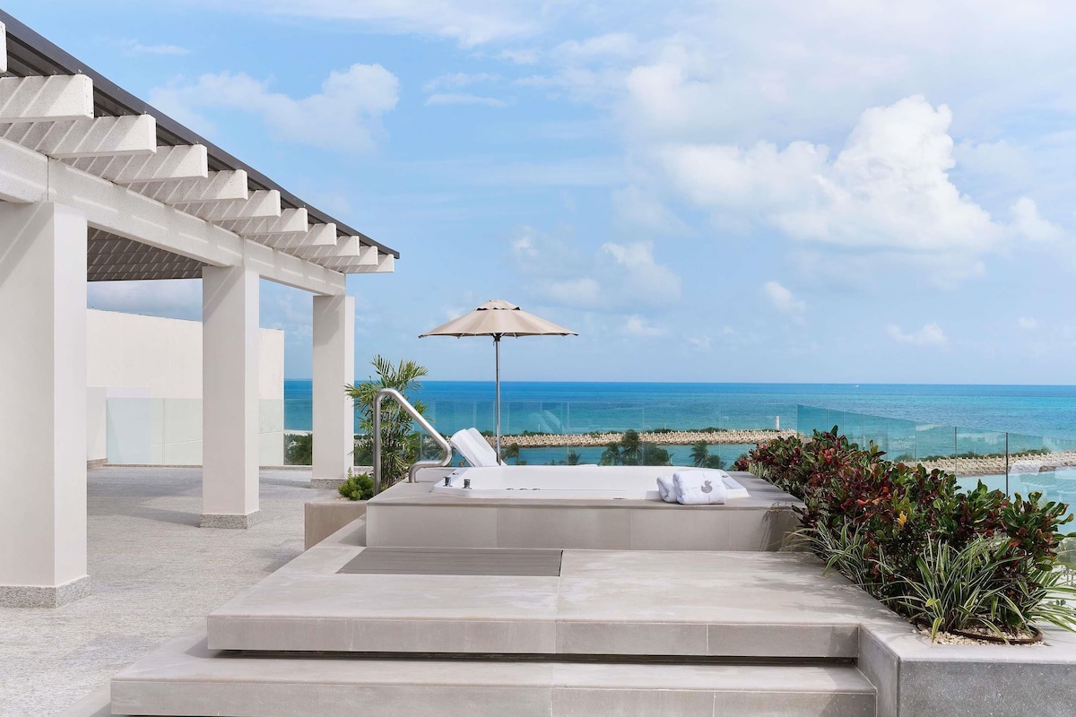 Un espacio lounge moderno al aire libre con piscina, sillones de descanso y vistas al océano.