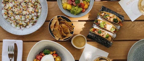 Una mesa con diversos platos, incluyendo tacos, una ensalada y un plato de rábanos en rodajas. También hay totopos, un cuenco pequeño de salsa y una copa de vino.