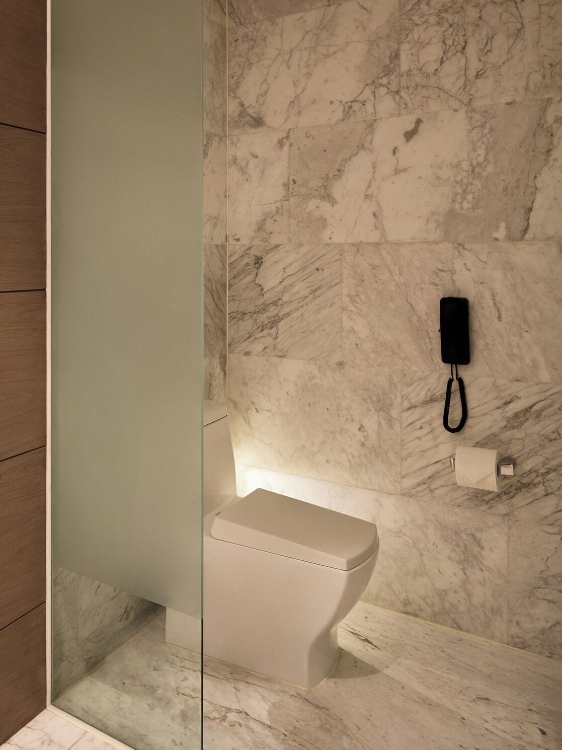 A modern bathroom with a marble wall, a toilet, and a glass partition.