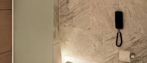 A modern bathroom with a marble wall, a toilet, and a glass partition.