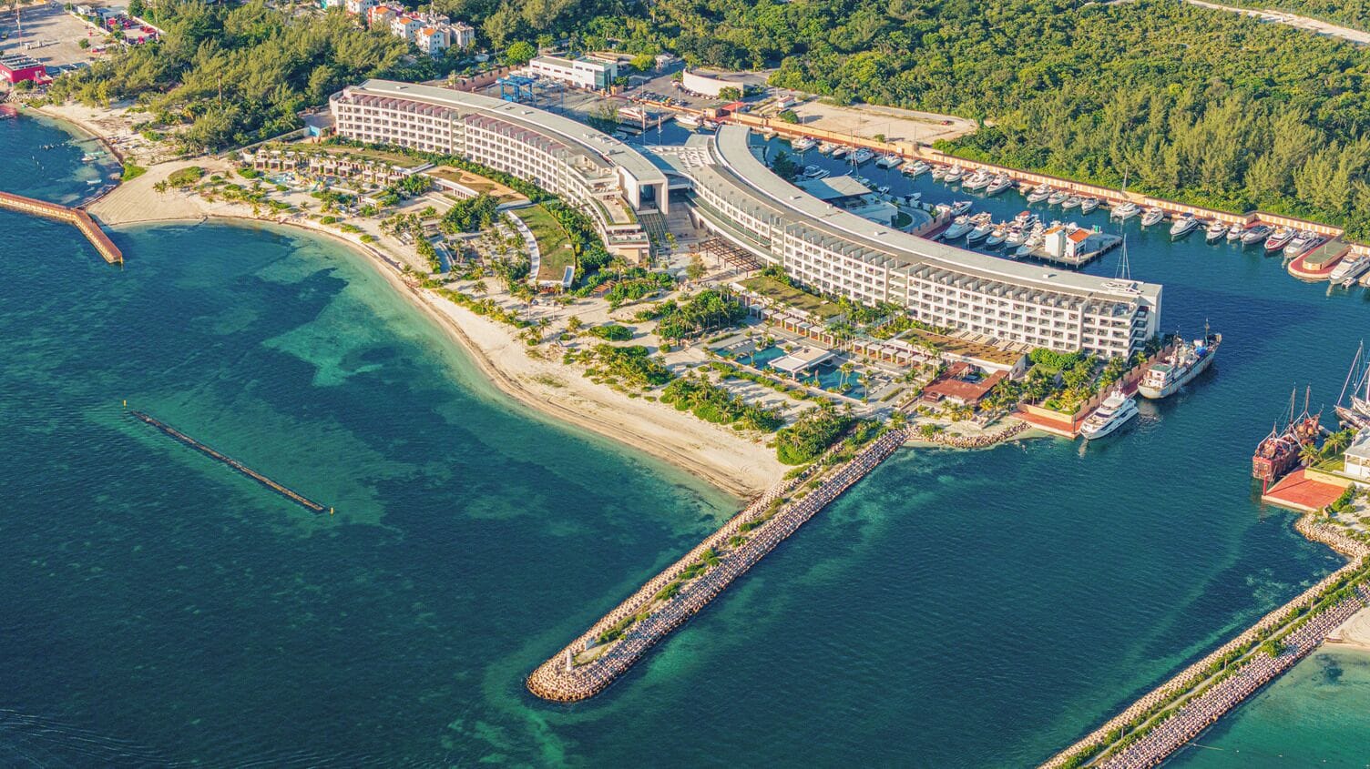 Luftaufnahme eines Küstenhotels mit einer Marina, einer langen Pier und einem Strand.