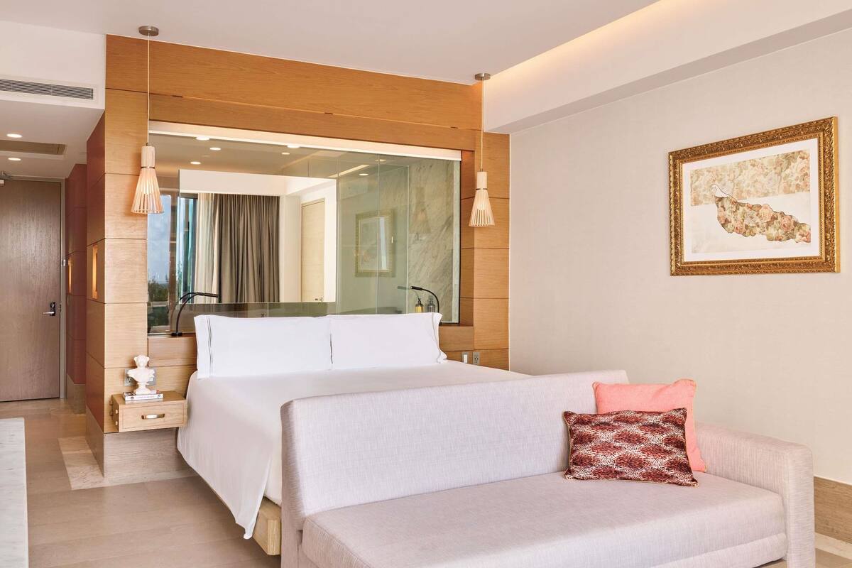 Una habitación de hotel moderna con una cama, un sofá, un espejo grande y un cuadro en la pared.