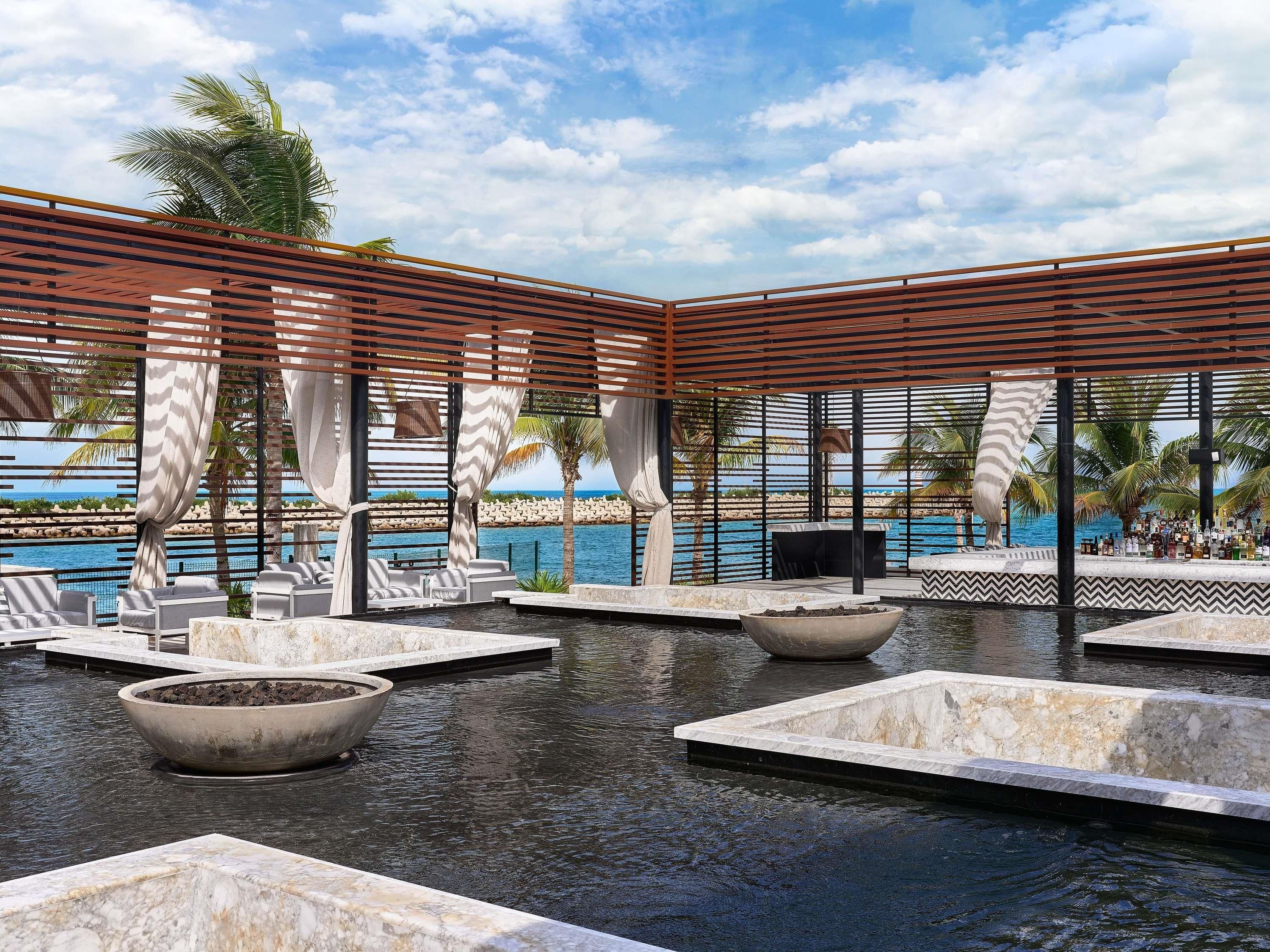 Zona de piscina con sillones de descanso, un bar y vistas al mar.