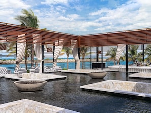 Zona de piscina con sillones de descanso, un bar y vistas al mar.