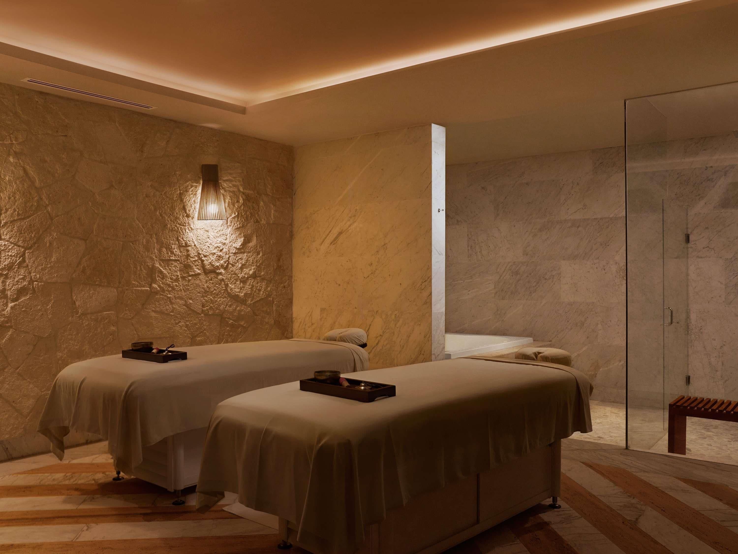 Une salle de spa équipée de deux lits, d’une table de massage, d’un banc et d’un mur en pierre.