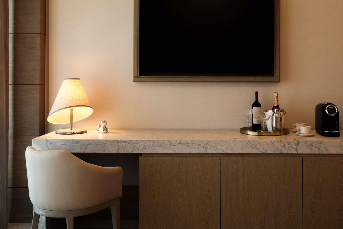A hotel bar area with a marble countertop, a lamp, a bottle of champagne, a coffee machine, and a chair.