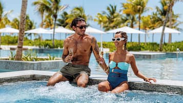 A couple in a hot tub with a pool and palm trees in the background.