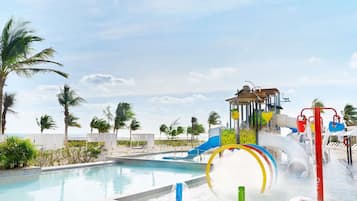 Relax by the clear blue pool surrounded by palm trees and a water play structure with multiple water jets and slides.